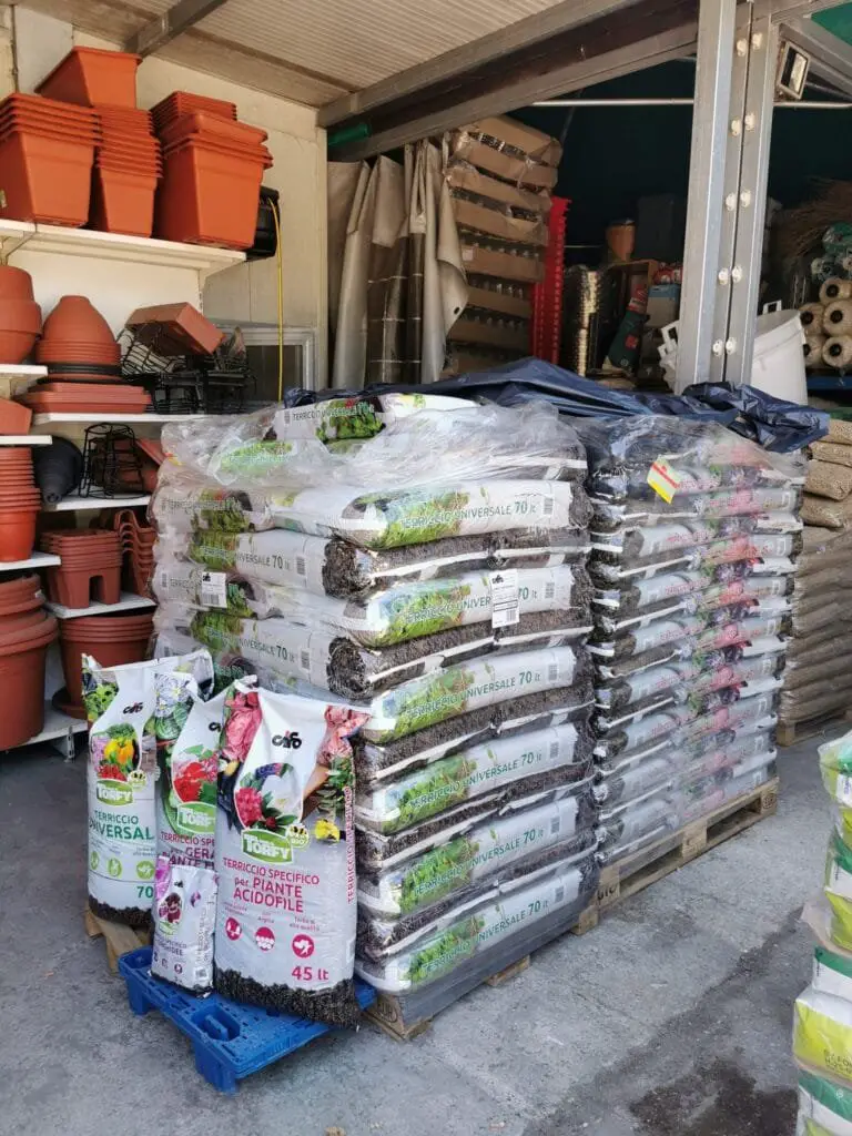 Coltivare l’Orto sul Balcone: Idee, Consigli e Piante Giuste 4 Scaffali con vasi in plastica e bancali di sacchi di terriccio universale in un centro per il giardinaggio, pronti per l’uso in coltivazione domestica.