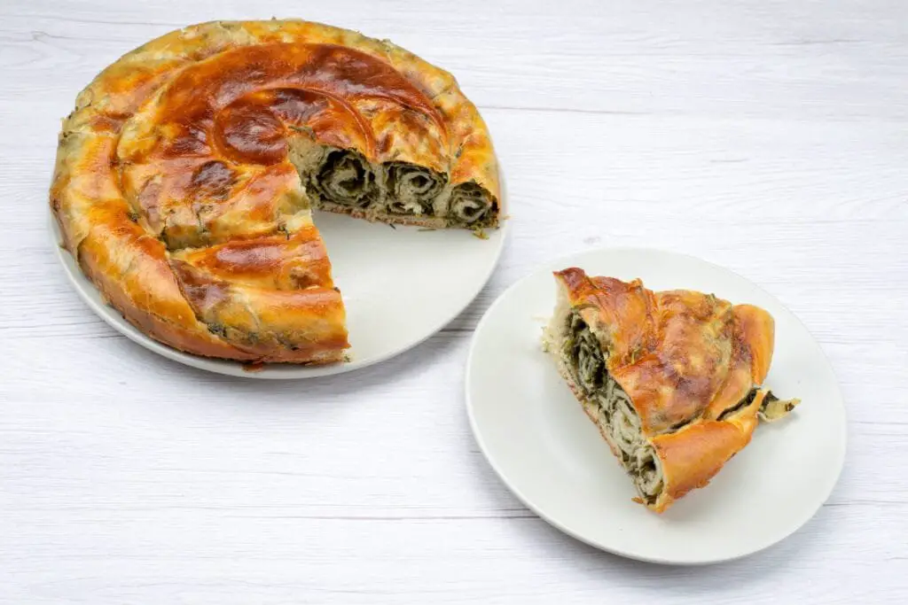 Borek Turco di Verdure: Ricetta Facile, Varianti e Consigli 2 Borek di verdure fatto in casa a spirale, una fetta servita su piattino bianco, ripieno verde di spinaci ben visibile nel taglio.