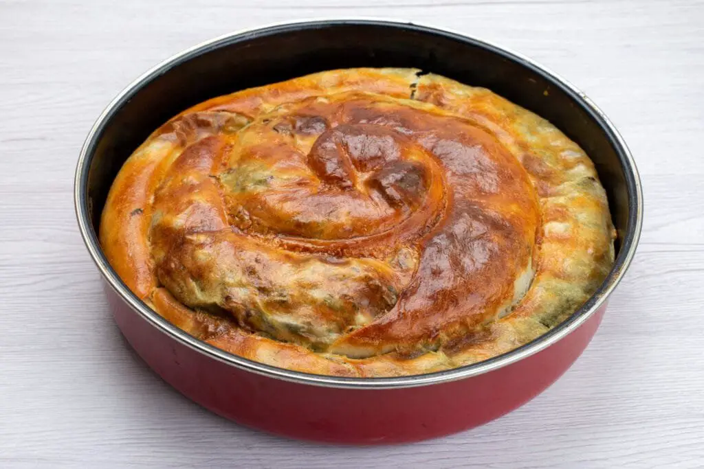 Borek Turco di Verdure: Ricetta Facile, Varianti e Consigli 3 Borek turco arrotolato cotto in teglia rotonda, superficie lucida e dorata, pronto da tagliare e servire.