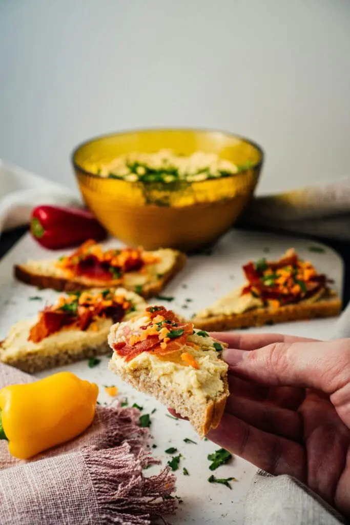 Hummus di Ceci Fatto in Casa: Ricetta Facile e Cremosa 5 Fette di pane spalmate con hummus di ceci e peperoni arrostiti, servite accanto a una ciotola di hummus