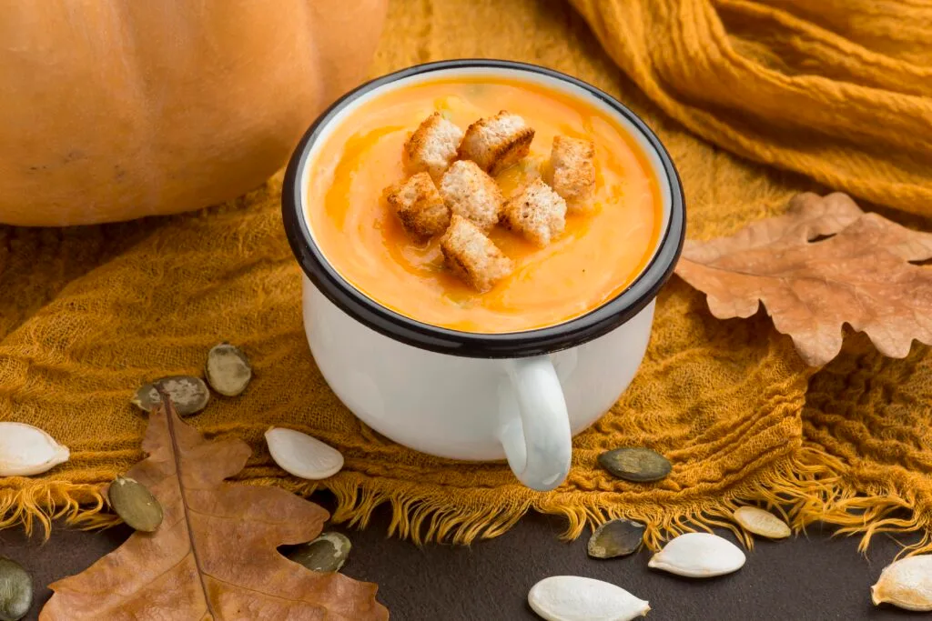 Corba di zucca turca: ingredienti, ricetta e coltivazione 5 Zuppa di zucca cremosa servita in una tazza smaltata bianca con crostini, decorazione autunnale.