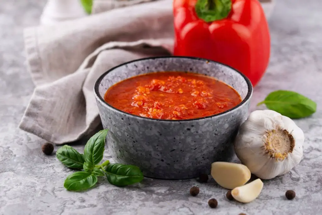 Ricetta Biber Salcasi: Come Fare la Salsa di Peperoni Turca 3 Ciotola di biber salcasi fatto in casa con peperoni rossi freschi, aglio e basilico sul tavolo.