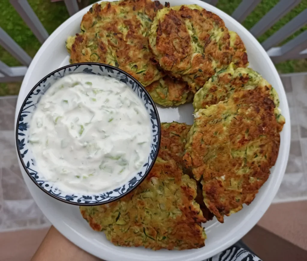Mucver: Frittelle di Zucchina Turche Ricetta e Varianti 2 Frittelle di zucchine mucver dorate servite con salsa yogurt cremosa in una ciotola