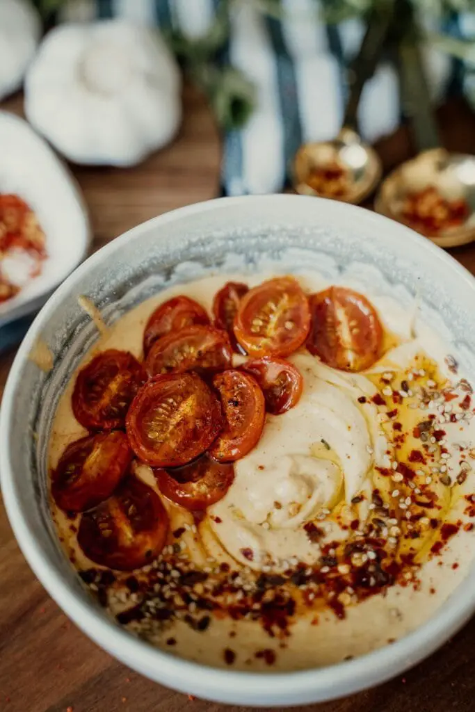 Hummus di Ceci Fatto in Casa: Ricetta Facile e Cremosa 6 Ciotola di hummus di ceci guarnita con pomodorini freschi a fette e peperoncino in polvere