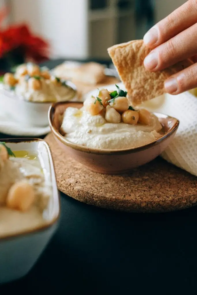 Hummus di Ceci Fatto in Casa: Ricetta Facile e Cremosa 7 Hummus di ceci cremoso servito in una ciotolina con ceci interi sopra e crostini