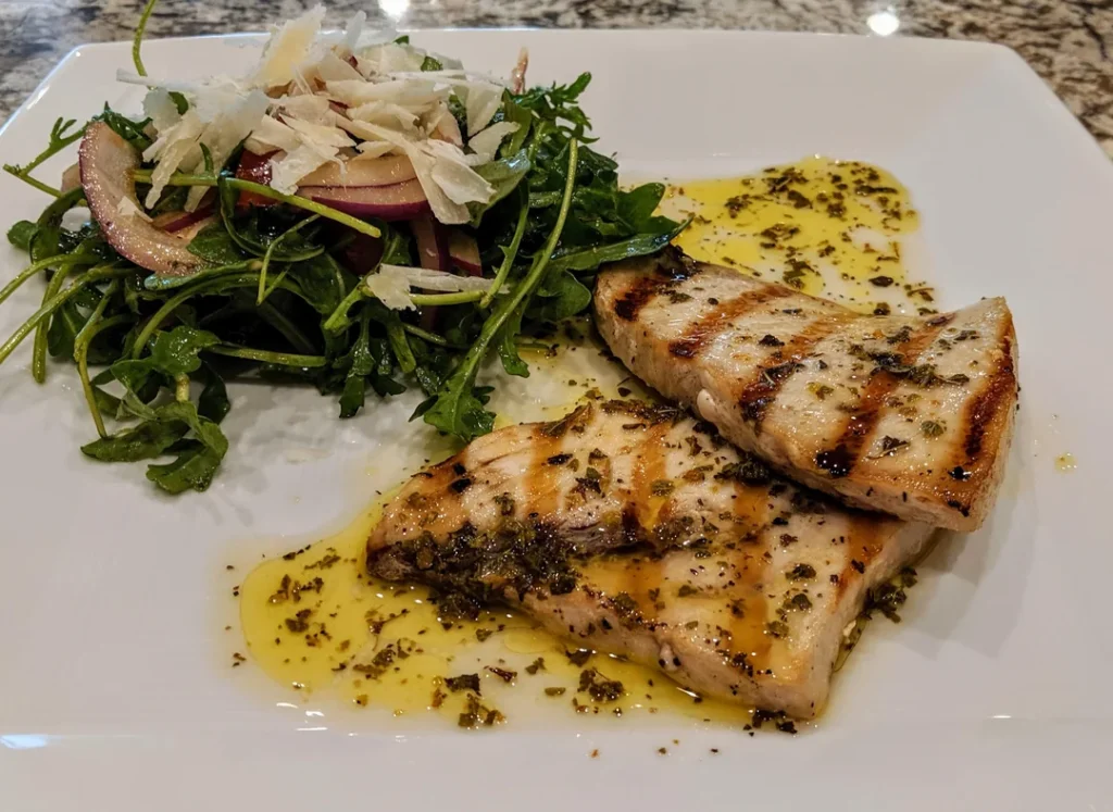 Salmoriglio Siciliano: Ricetta, Usi e Ingredienti Freschi 5 Tranci di pesce grigliato con salmoriglio siciliano fatto in casa, accompagnati da insalata di rucola e cipolla rossa dell’orto, un pranzo semplice che preparo d’estate