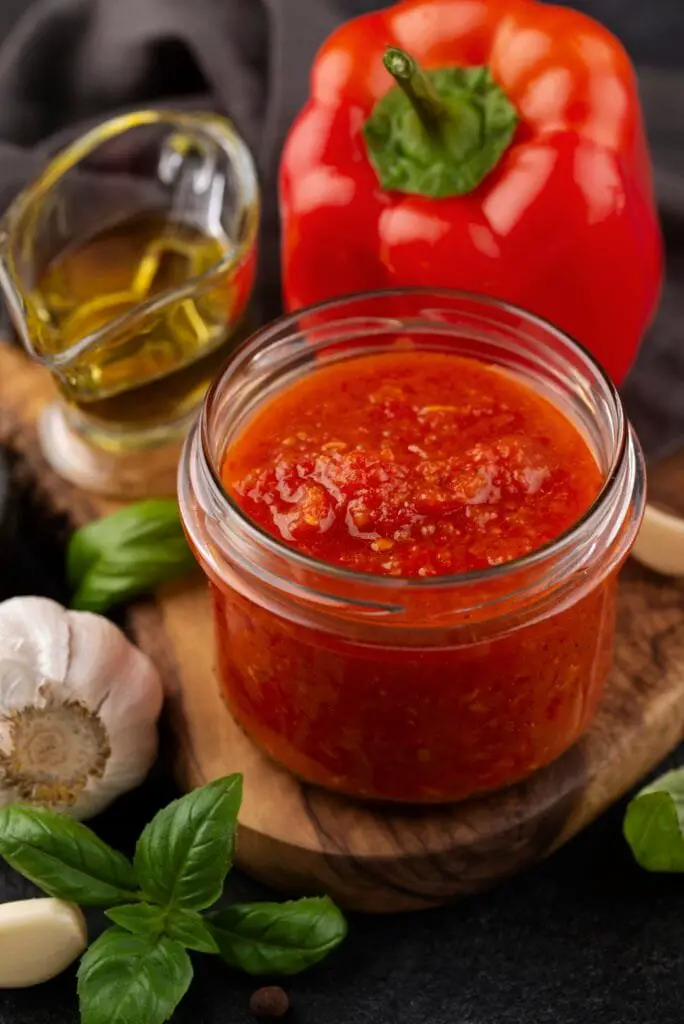 Ricetta Biber Salcasi: Come Fare la Salsa di Peperoni Turca 1 Biber salcasi in barattolo con ingredienti freschi: peperone rosso, aglio e basilico su sfondo rustico.